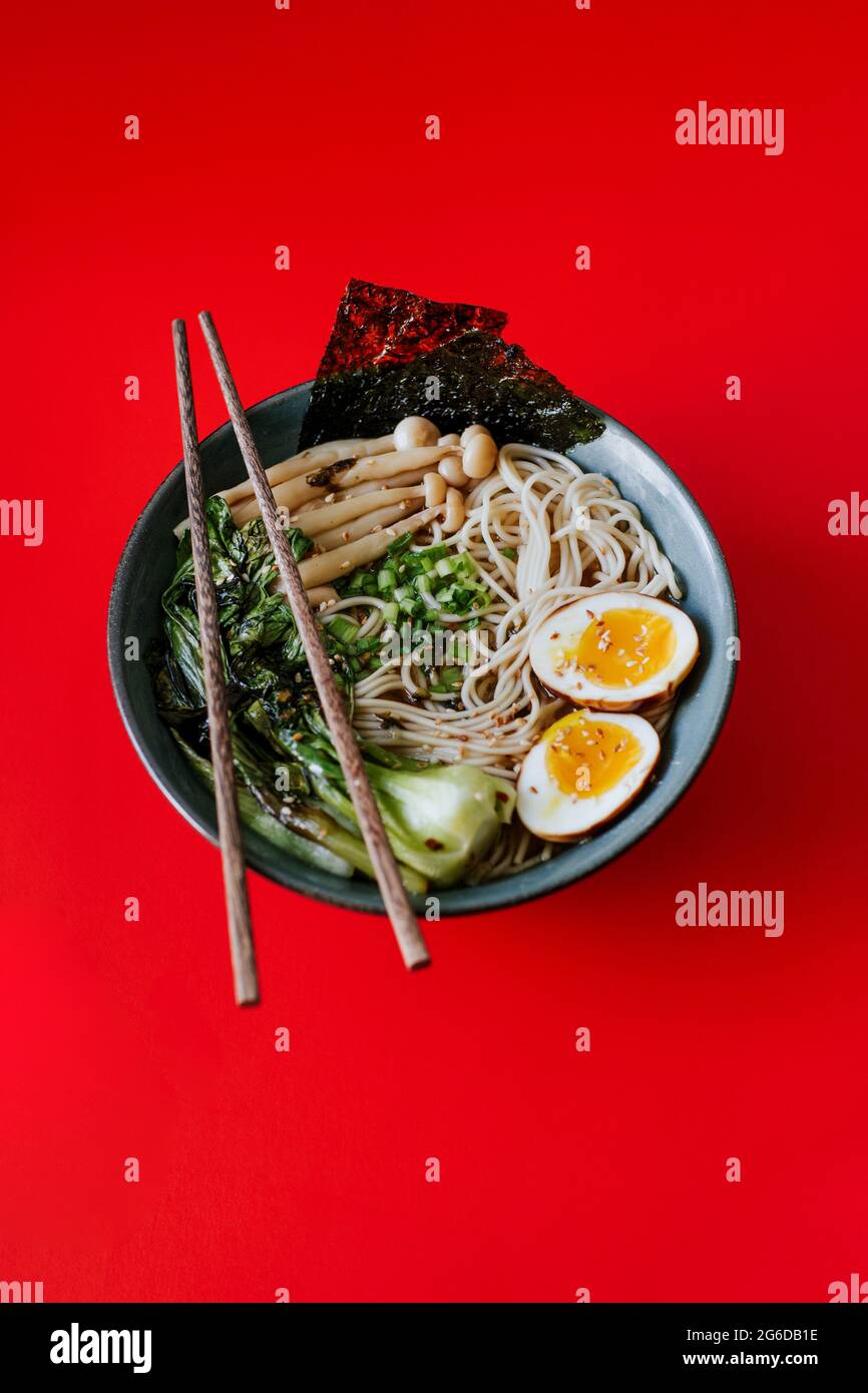 Vista dall'alto della ciotola in ceramica con deliziosi ramen e bastoncini posizionati su sfondo rosso Foto Stock