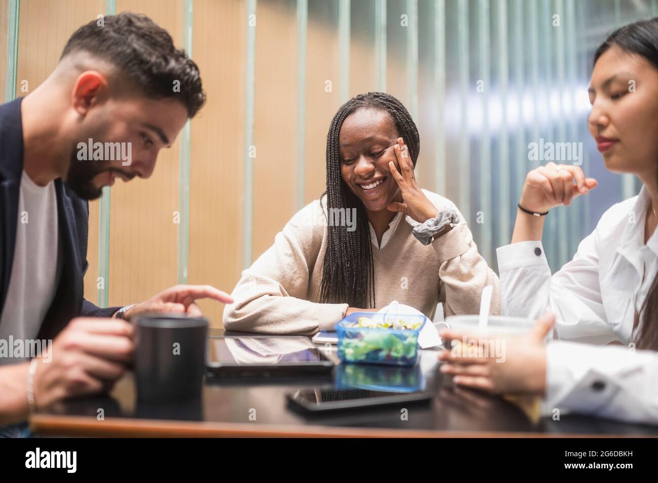 Compagnia di diversi colleghi che si riuniscono al tavolo in cucina e che si rompono mentre si mangia il pranzo Foto Stock