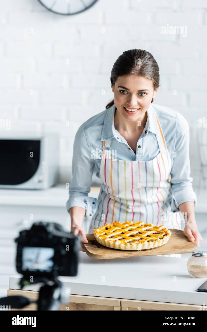 macchina fotografica digitale sfocata vicino blogger culinario felice che tiene torta gustosa Foto Stock