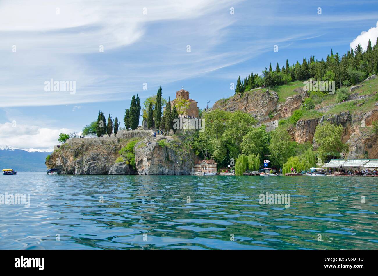 Splendida vista dal lago con barche albero, pietre, spiaggia, montagna su cielo azzurro Foto Stock