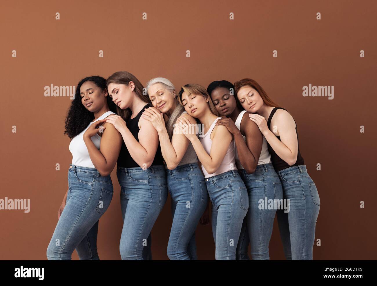 Donne diverse in casual abbracciarsi mentre si levano in piedi con occhi chiusi su sfondo marrone Foto Stock