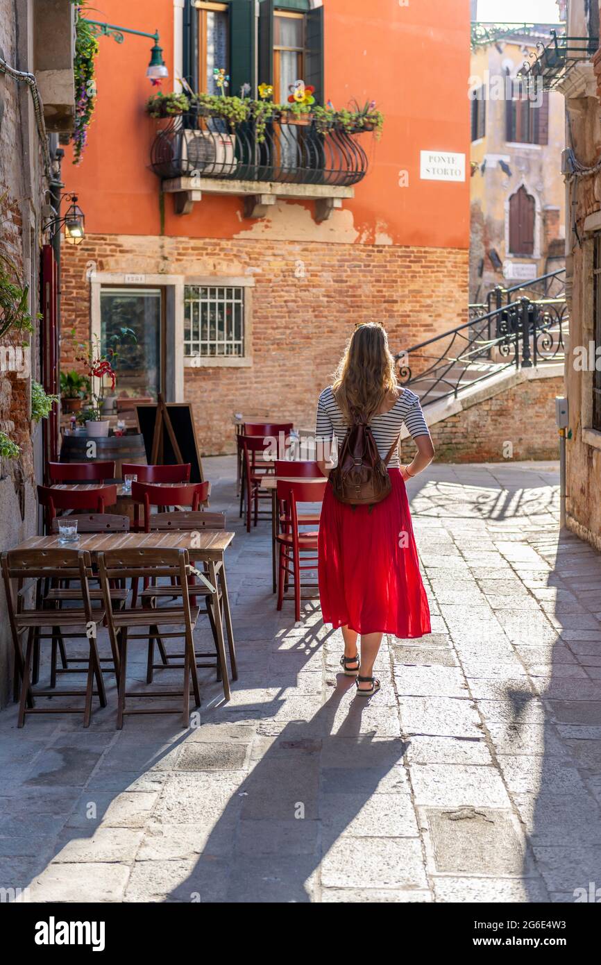 Giovane donna in abito rosso camminando attraverso vicolo stretto, Venezia, Veneto, Italia Foto Stock