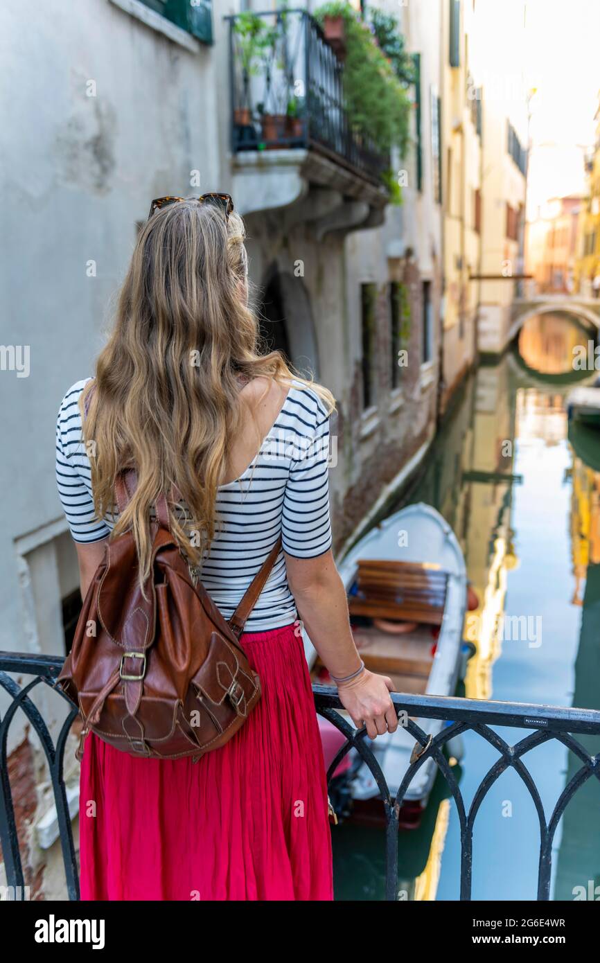 Giovane donna in abito rosso che guarda canale, Venezia, Veneto, Italia Foto Stock