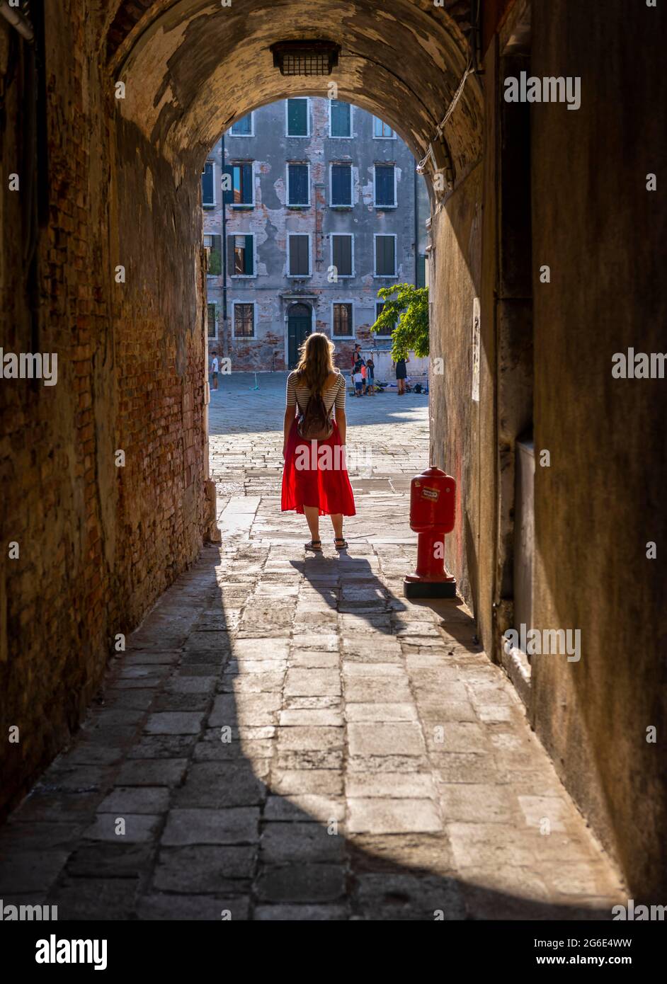 Giovane donna in abito rosso camminando attraverso vicolo stretto, Venezia, Veneto, Italia Foto Stock