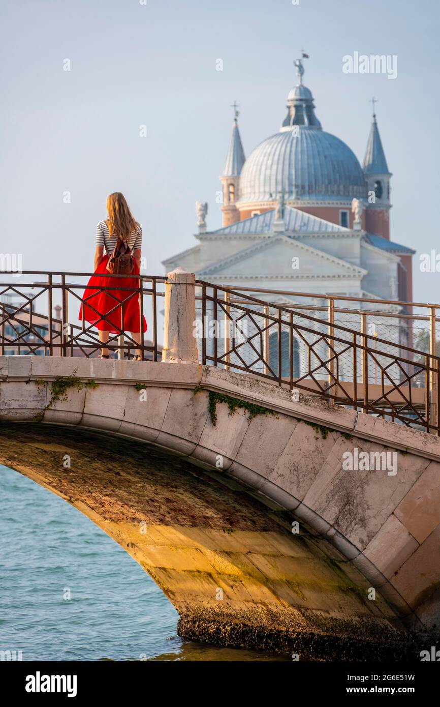 Giovane donna in abito rosso su un ponte su un canale, nella chiesa posteriore del Santissimo Redentore, Venezia, Veneto, Italia Foto Stock