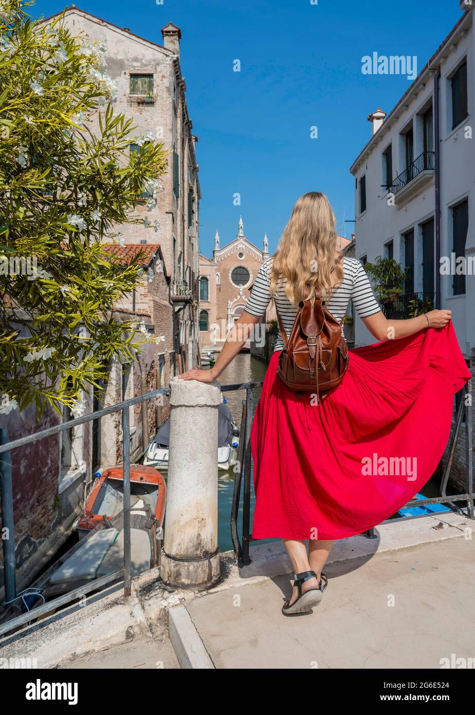 Giovane donna in abito rosso che si affaccia su un canale, Venezia, Veneto, Italia Foto Stock