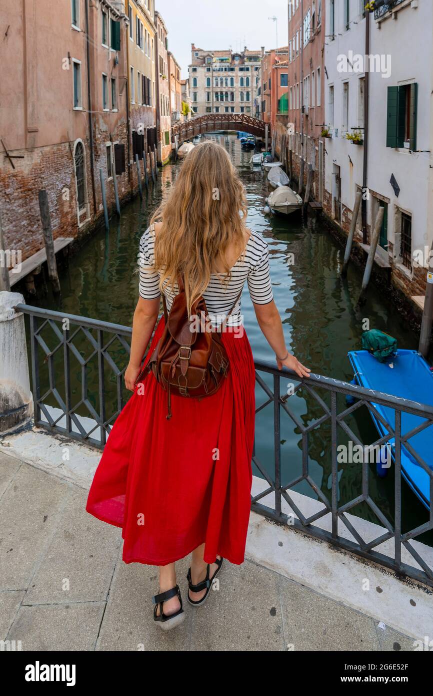 Giovane donna in abito rosso che si affaccia su un canale, Venezia, Veneto, Italia Foto Stock