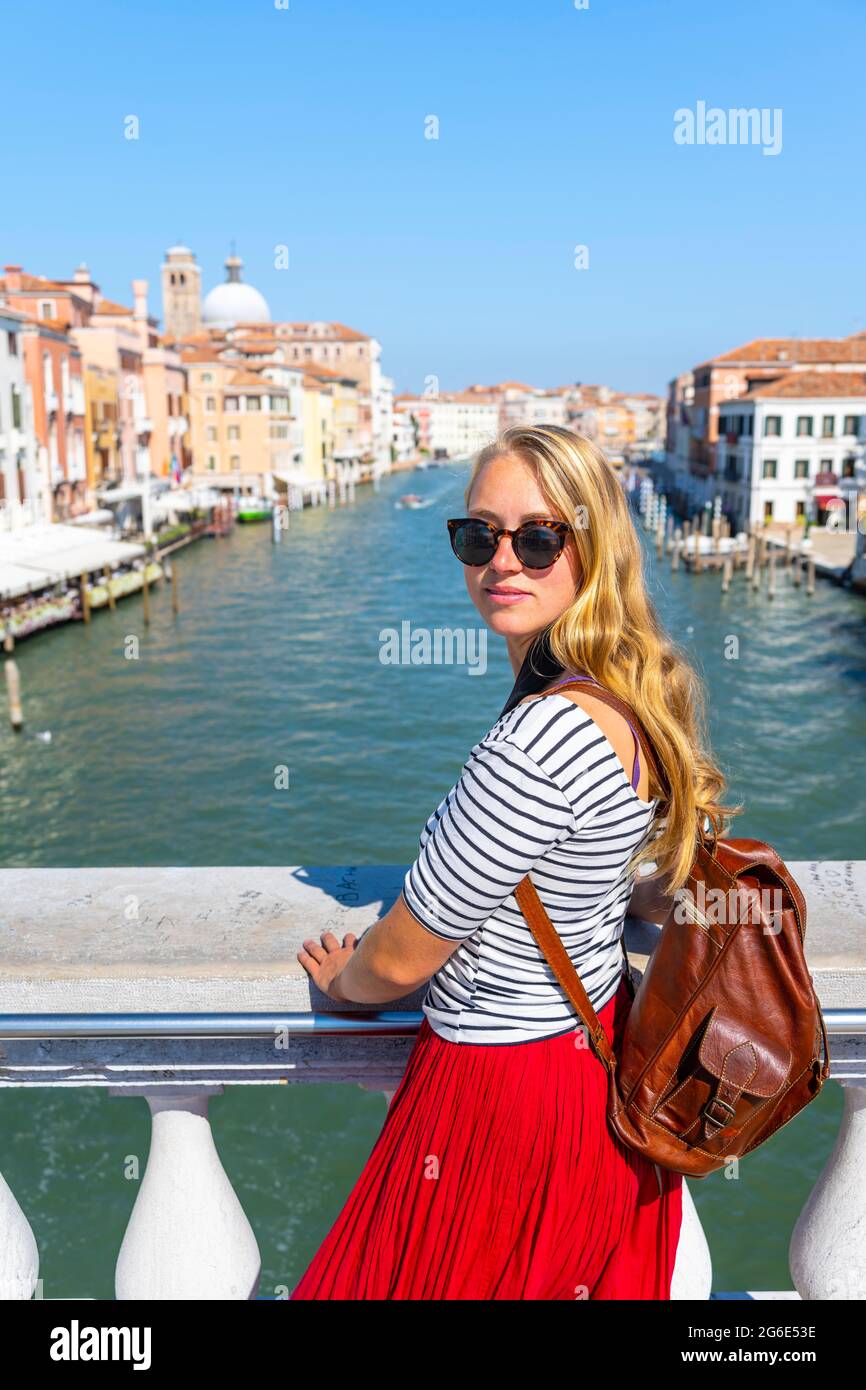 Giovane donna in abito rosso guarda alla macchina fotografica, Ponte Scalzi sul Canal Grande, Venezia, Veneto, Italia Foto Stock