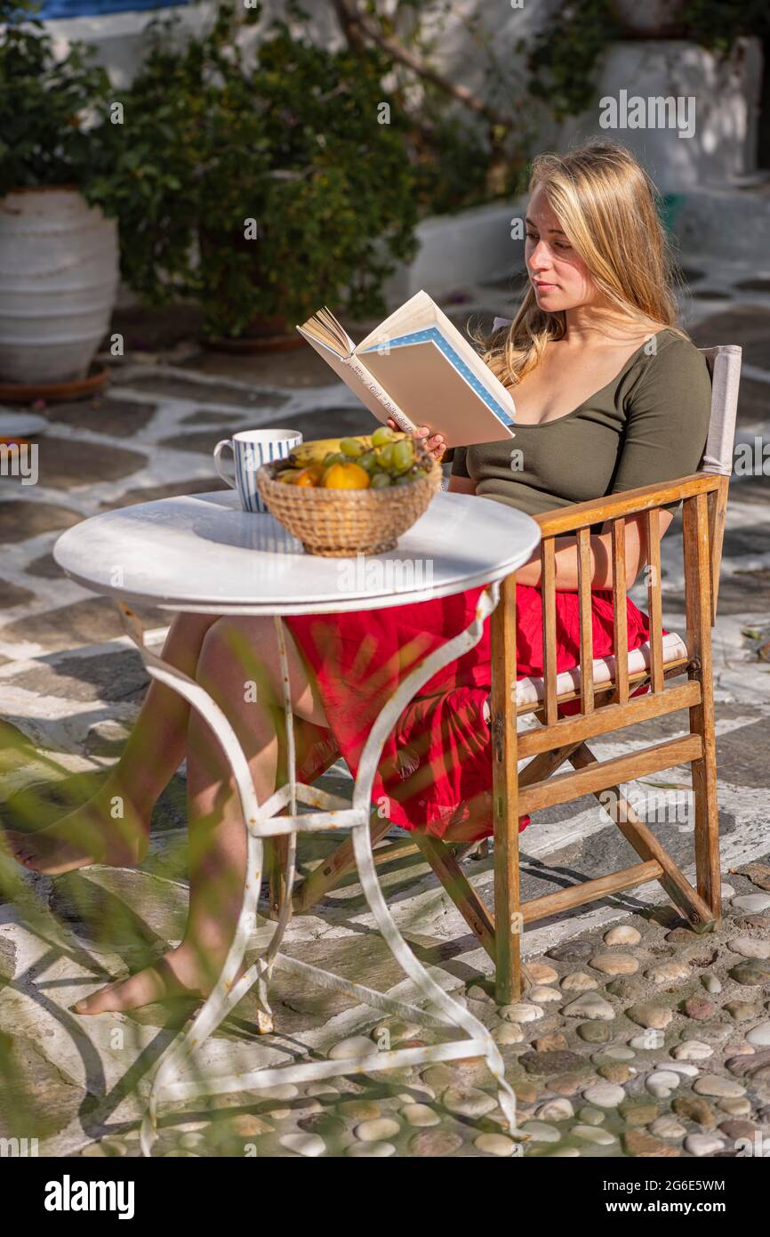 Giovane donna che legge un libro, prima colazione in vacanza, cortile, Grecia Foto Stock