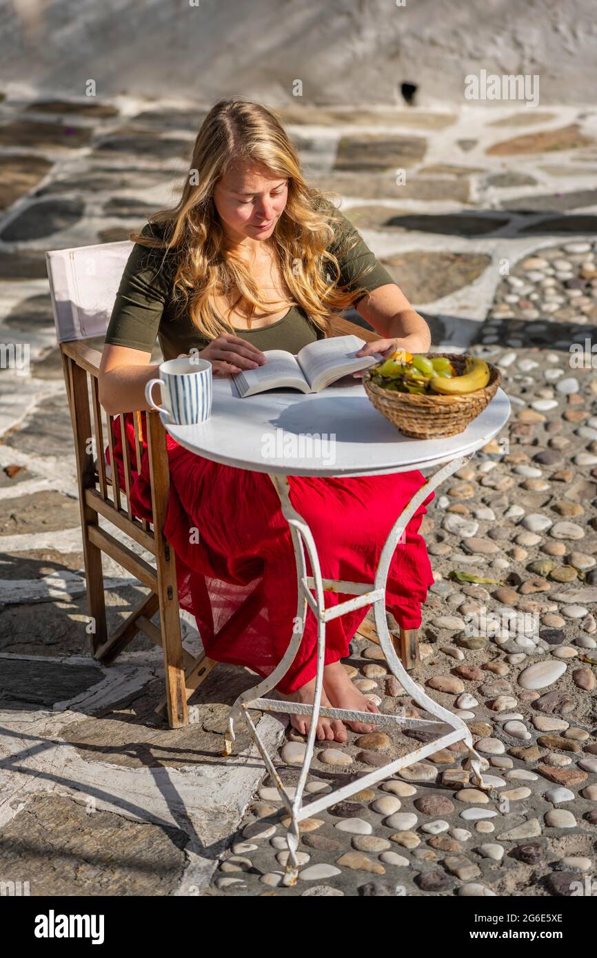 Giovane donna che legge, prima colazione in vacanza, cortile, Grecia Foto Stock