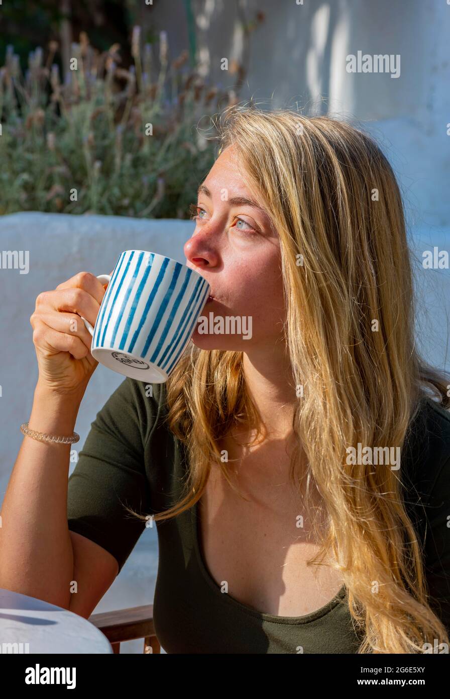 Giovane donna che beve da una tazza, colazione in vacanza fuori, Grecia Foto Stock