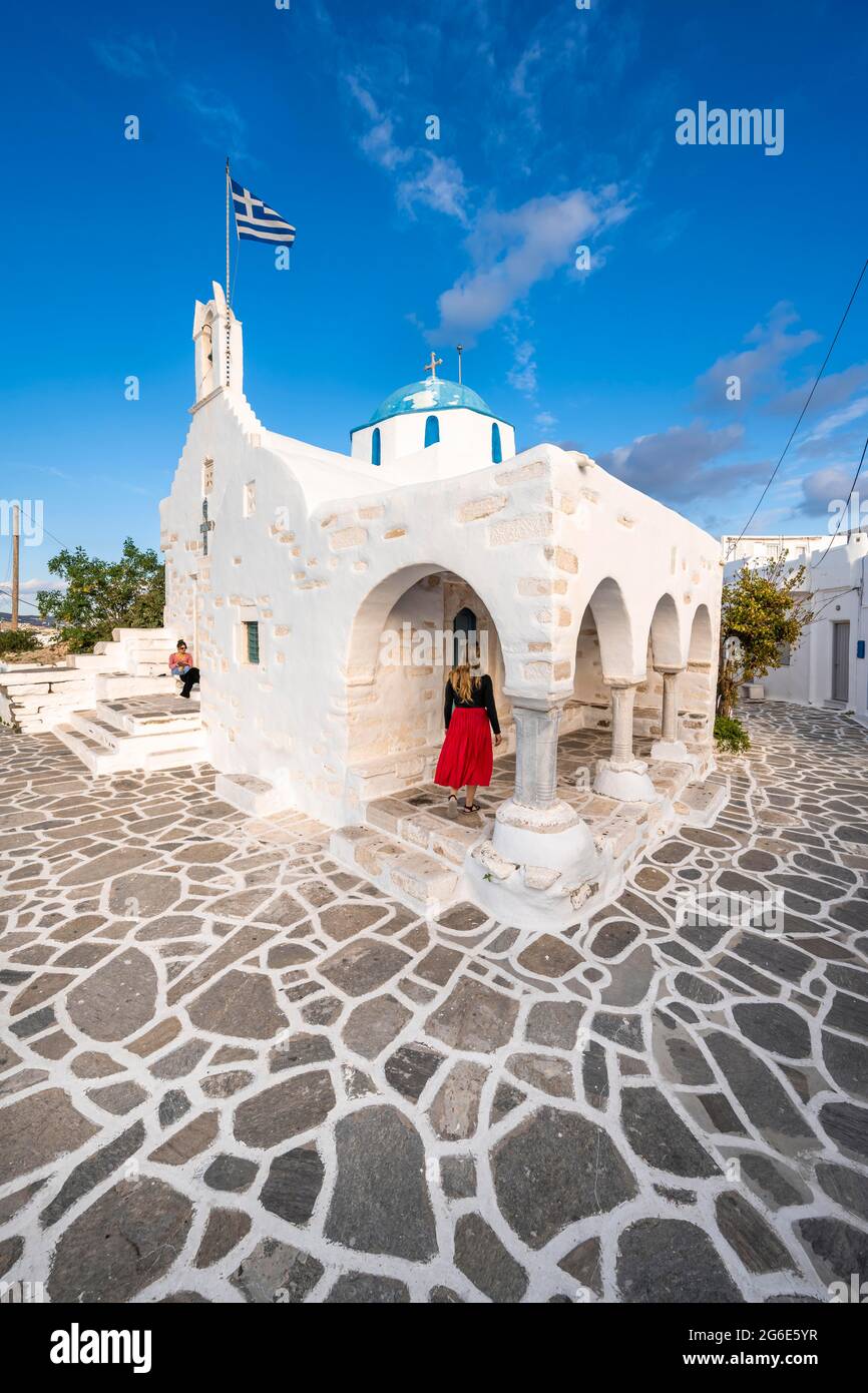 Turismo con abito rosso, blu e bianco greco ortodosso Chiesa Agios Nikolaos con bandiera greca, Parikia, Paros, Cicladi, Mar Egeo, Grecia Foto Stock
