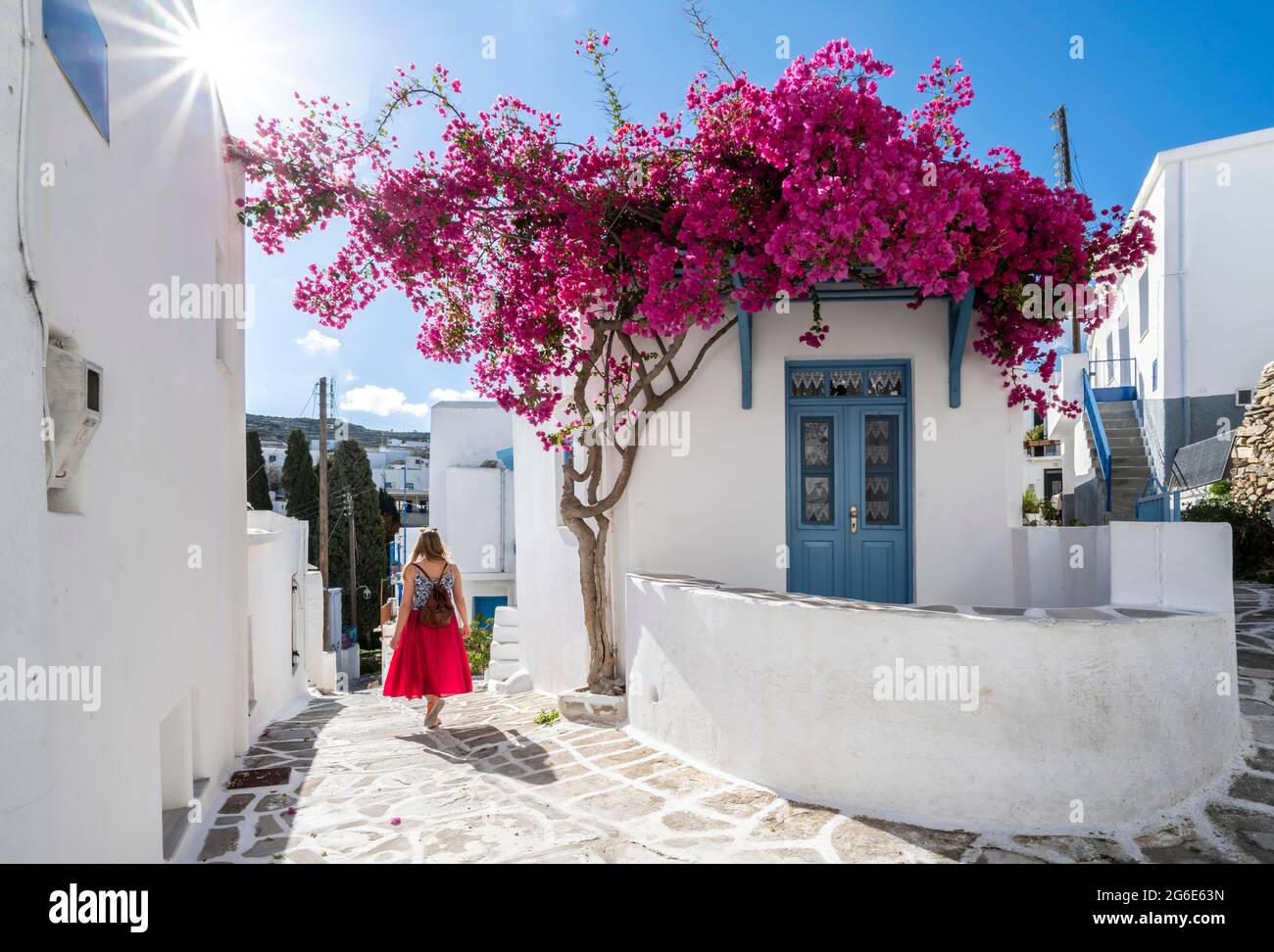 Bianco-blu case con fiore viola Bougainvillea (Bougainvillea), giovane donna con abito rosso nel centro storico di Lefkes, Paros, Cicladi, Grecia Foto Stock