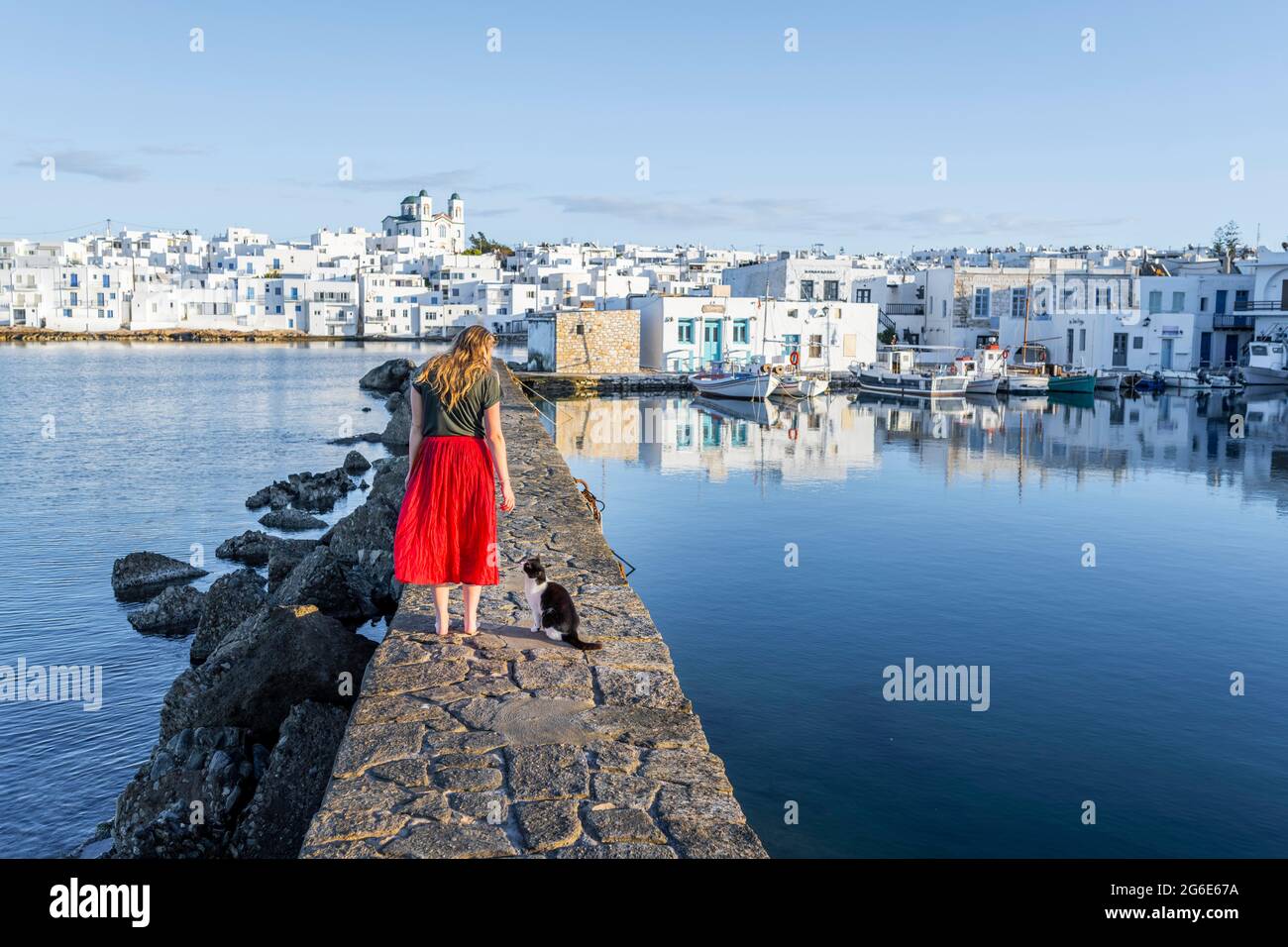 Gatto e giovane donna con abito rosso sulla parete del porto, dietro la chiesa di Naoussa, città portuale Naoussa, isola Paros, Cicladi, Grecia Foto Stock