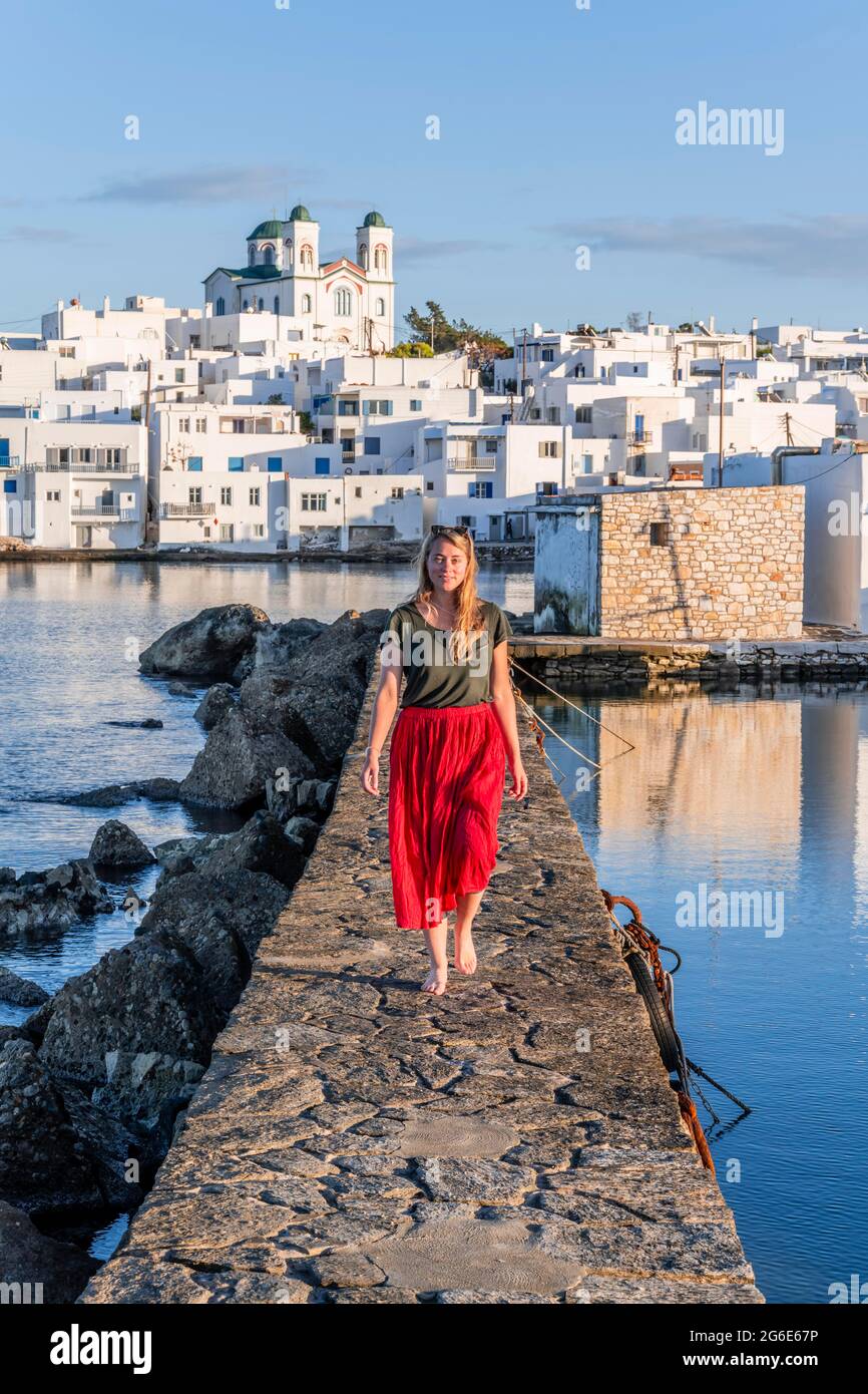 Giovane donna con abito rosso sulla parete del porto, dietro la chiesa di Naoussa, città portuale Naoussa, isola Paros, Cicladi, Grecia Foto Stock