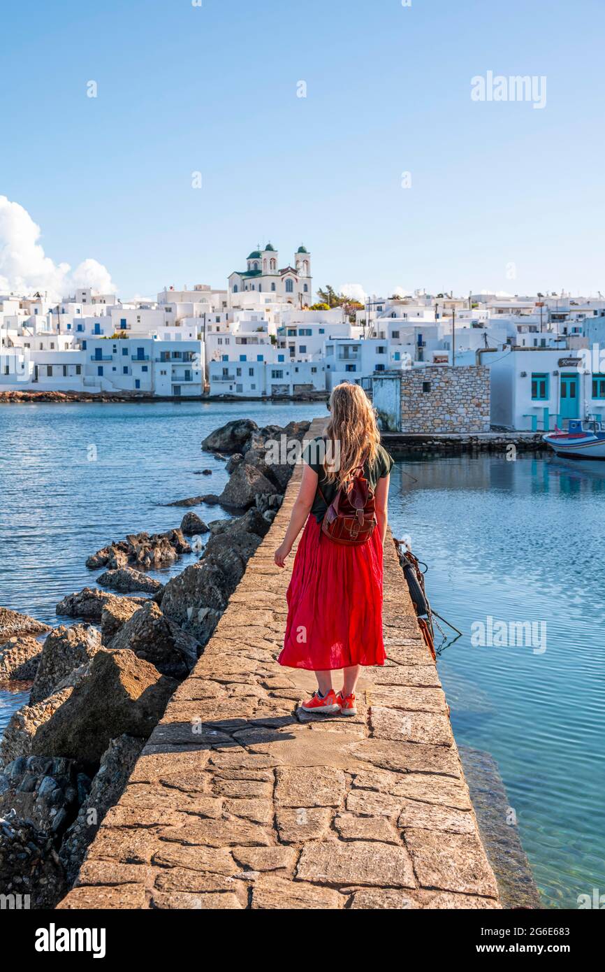 Giovane donna con abito rosso sulla parete del porto, città portuale Naoussa, isola Paros, Cicladi, Grecia Foto Stock