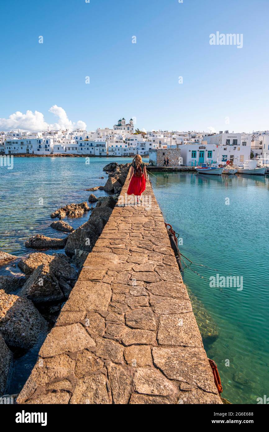 Giovane donna con abito rosso sulla parete del porto, città portuale Naoussa, isola Paros, Cicladi, Grecia Foto Stock