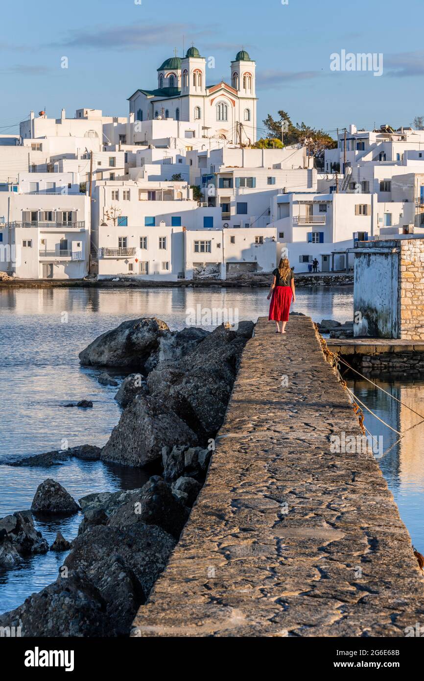 Giovane donna con abito rosso sulla parete del porto, dietro la chiesa di Naoussa, città portuale Naoussa, isola Paros, Cicladi, Grecia Foto Stock