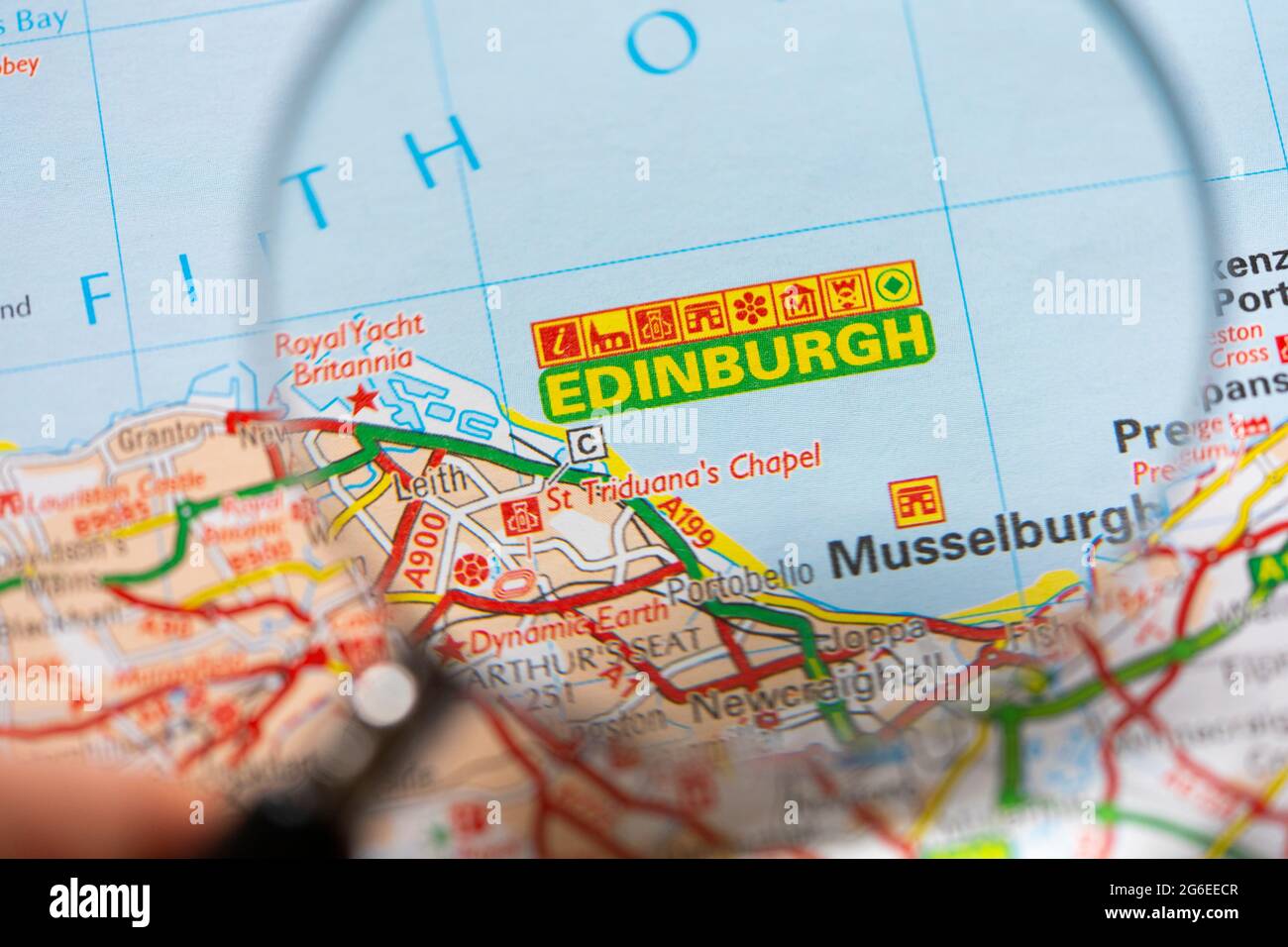 Primo piano di una pagina in un atlante della carta stradale stampata con una mano dell'uomo che tiene una lente di ingrandimento che mostra un allargamento della capitale della Scozia - Edimburgo Foto Stock