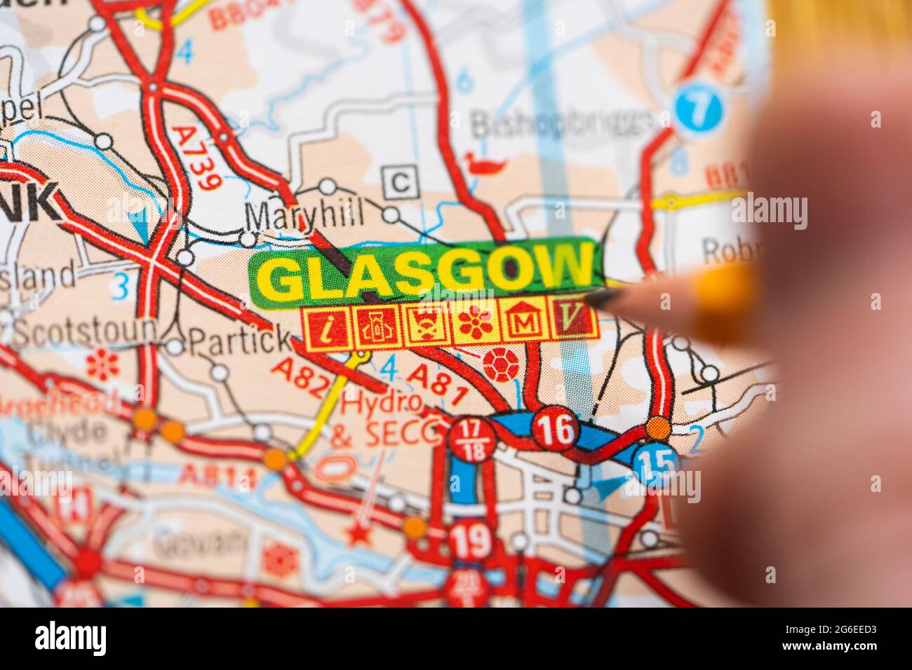 Macro closeup di una pagina in una carta stradale stampata atlante con una mano di un uomo che tiene una matita che punta alla città scozzese di Glasgow Foto Stock