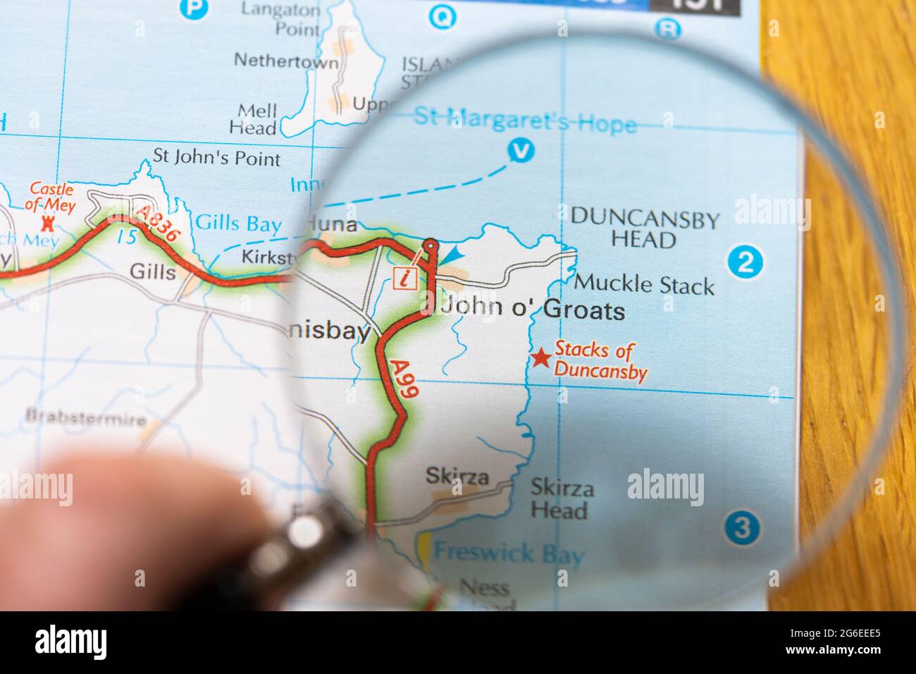 Primo piano di un atlante con carta stradale stampata con una lente d'ingrandimento che mostra un ingrandimento di John o'Groats, il villaggio più popolato a nord della Scozia Foto Stock
