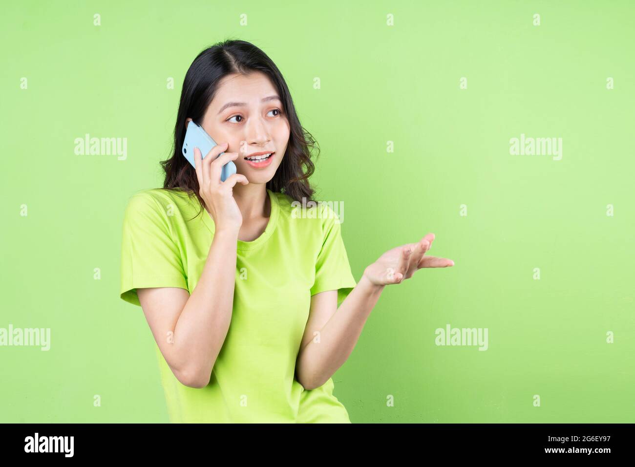 Immagine della giovane donna asiatica che tiene uno smartphone su sfondo verde Foto Stock