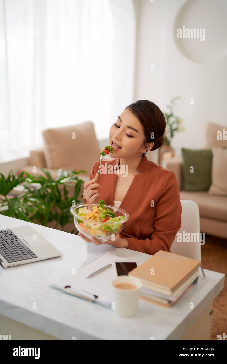 Ritratto di donna che guarda il film sul computer portatile e che mangia insalata di verdure a tavola in pausa Foto Stock