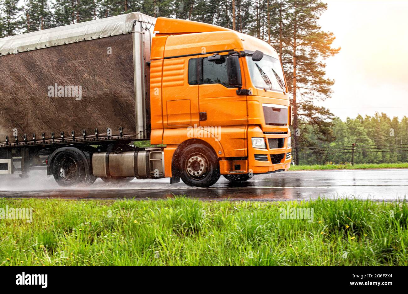 il moderno veicolo arancione con semi-rimorchio guida su una strada bagnata sotto la pioggia. Strada sdrucciolevole, aderenza degli pneumatici Foto Stock