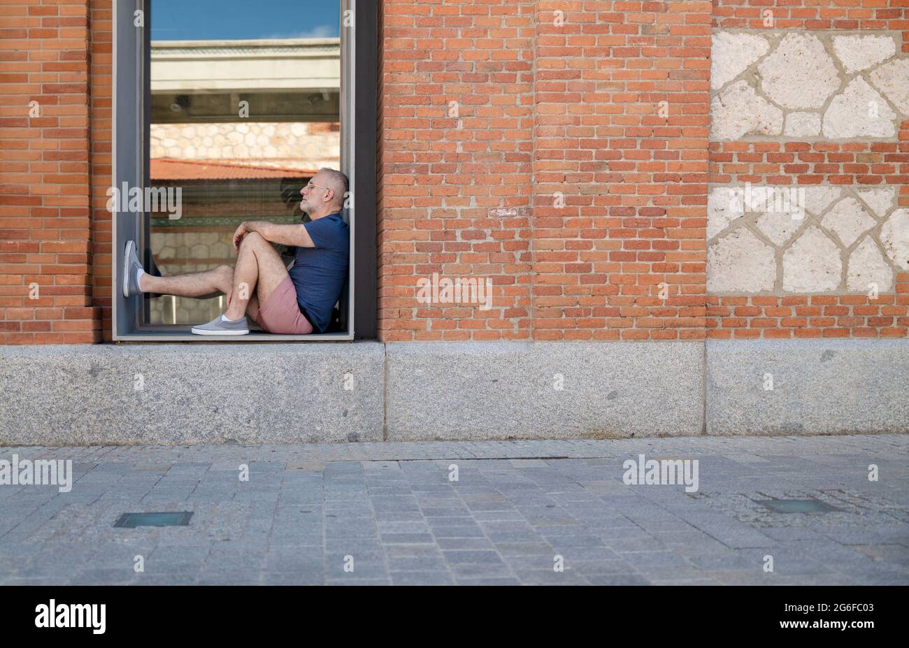 Uomo che dormiva nella finestra di un edificio pubblico Foto Stock