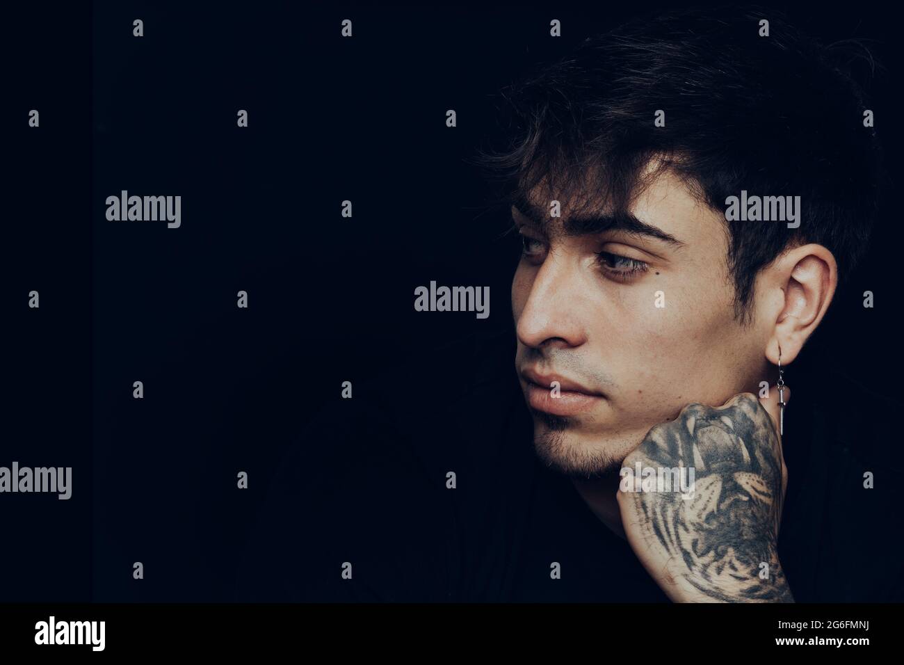 Giovane uomo con tatuaggi e orecchini che guardano da parte con  un'espressione penosa Foto stock - Alamy