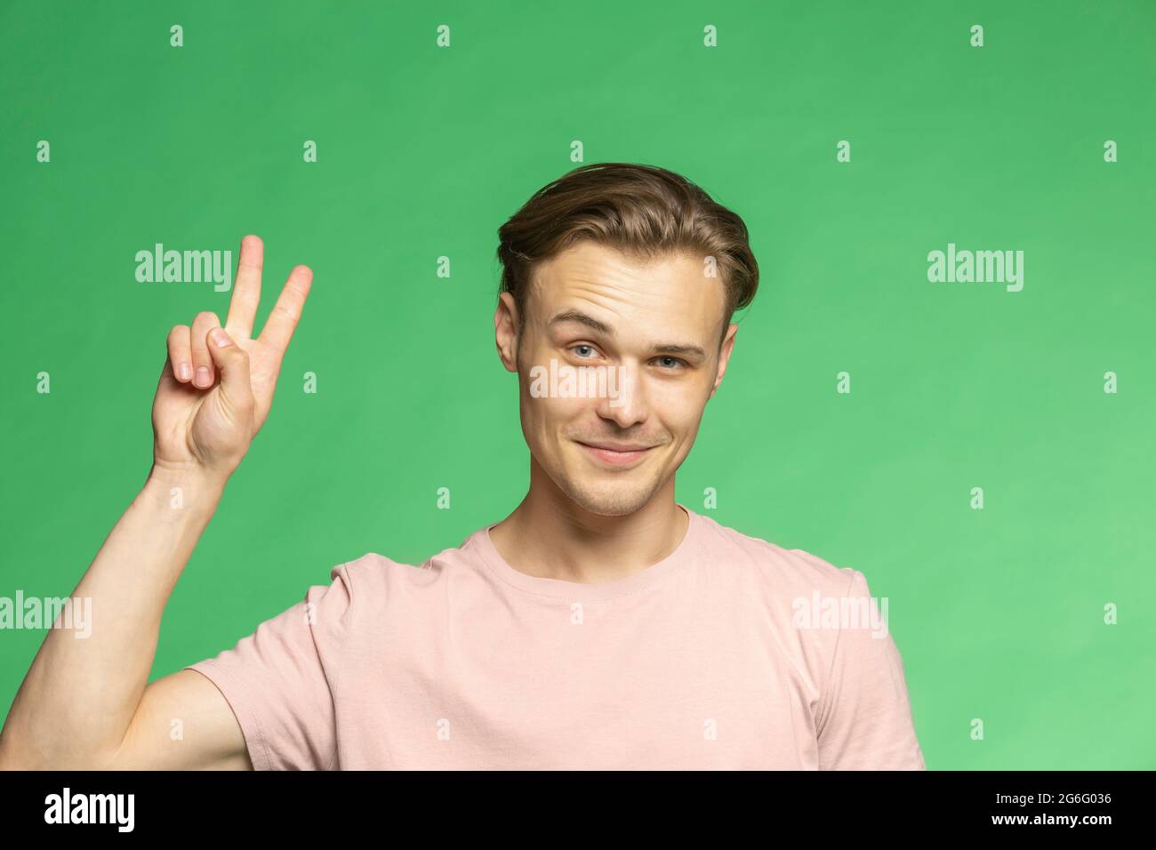Ritratto sicuro giovane uomo gesturing segno di pace su sfondo verde Foto Stock