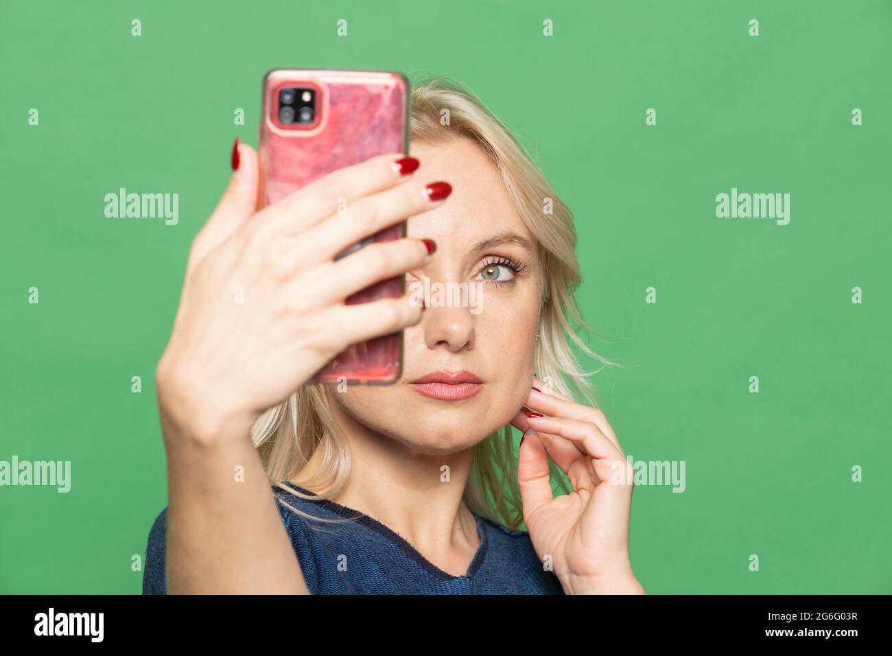 Bella donna bionda che prende selfie su sfondo verde Foto Stock