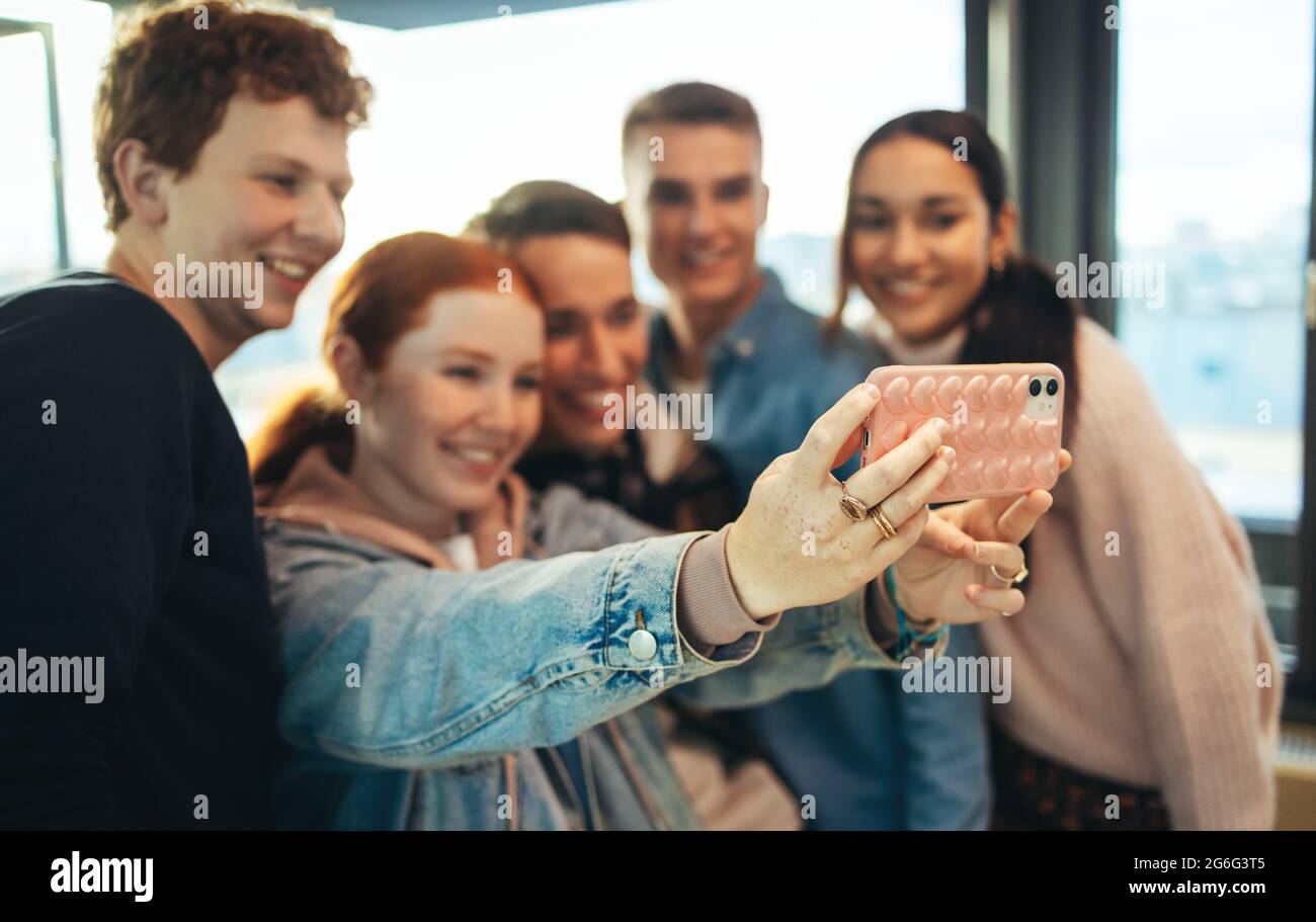 Ragazza che prende selfie con i suoi amici a scuola superiore. Gruppo di scuola superiore che prende selfie. Foto Stock