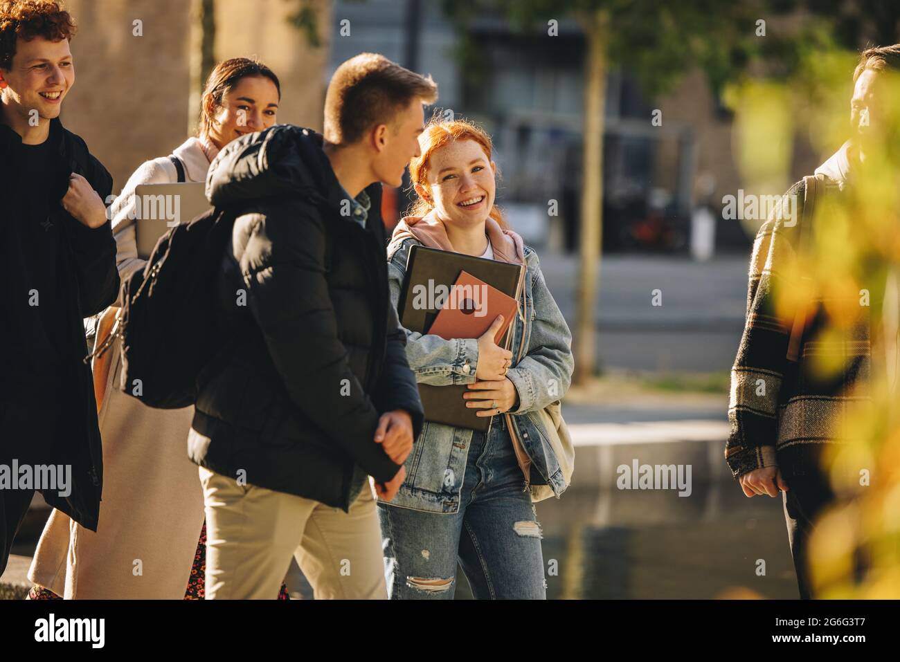 Ragazza sorridente che cammina con gli amici all'esterno a scuola superiore. Studenti allegri che camminano insieme dopo la lezione nel campus universitario Foto Stock