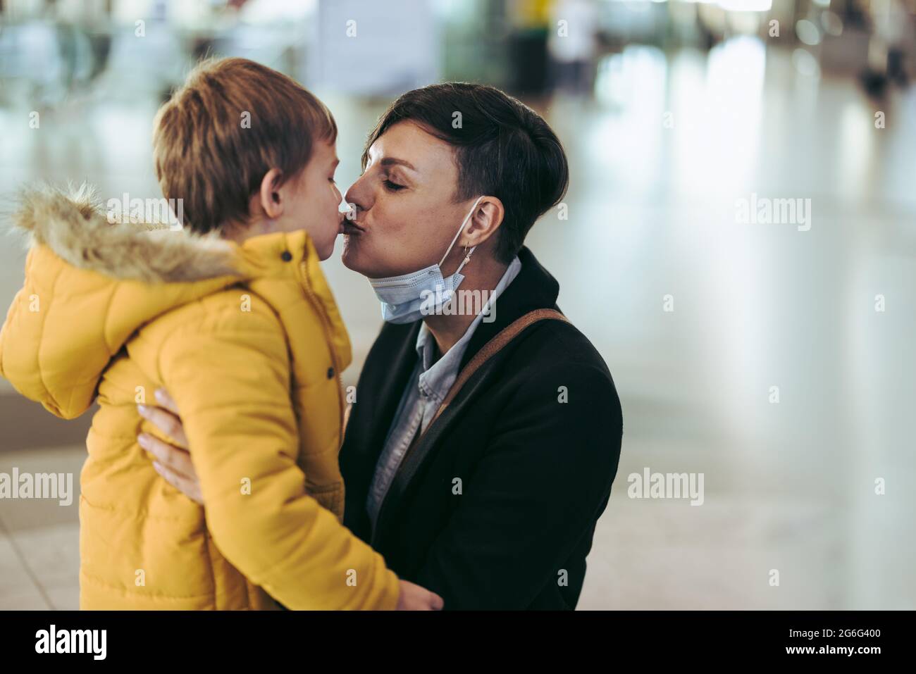 Donna che baciava il figlio all'aeroporto. Madre incontrando il suo bambino dopo lunga separazione durante l'epidemia di virus corona. Foto Stock