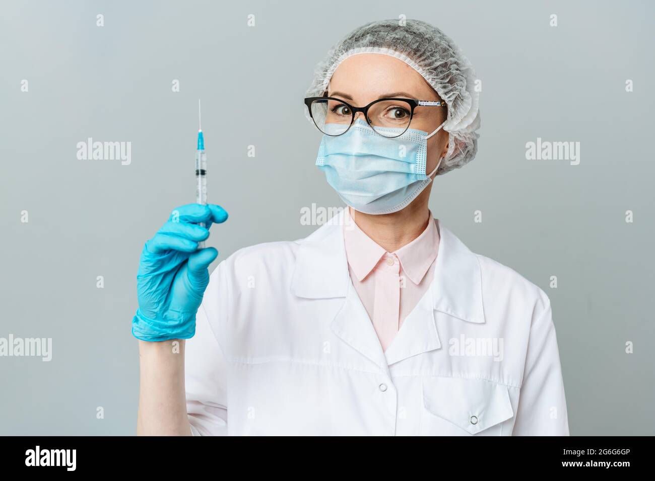 Medico donna o scienziato in bianco camice blu, guanti, cappuccio verde e la maschera contiene una siringa in mani su sfondo bianco. Ella è pronta a dare Foto Stock