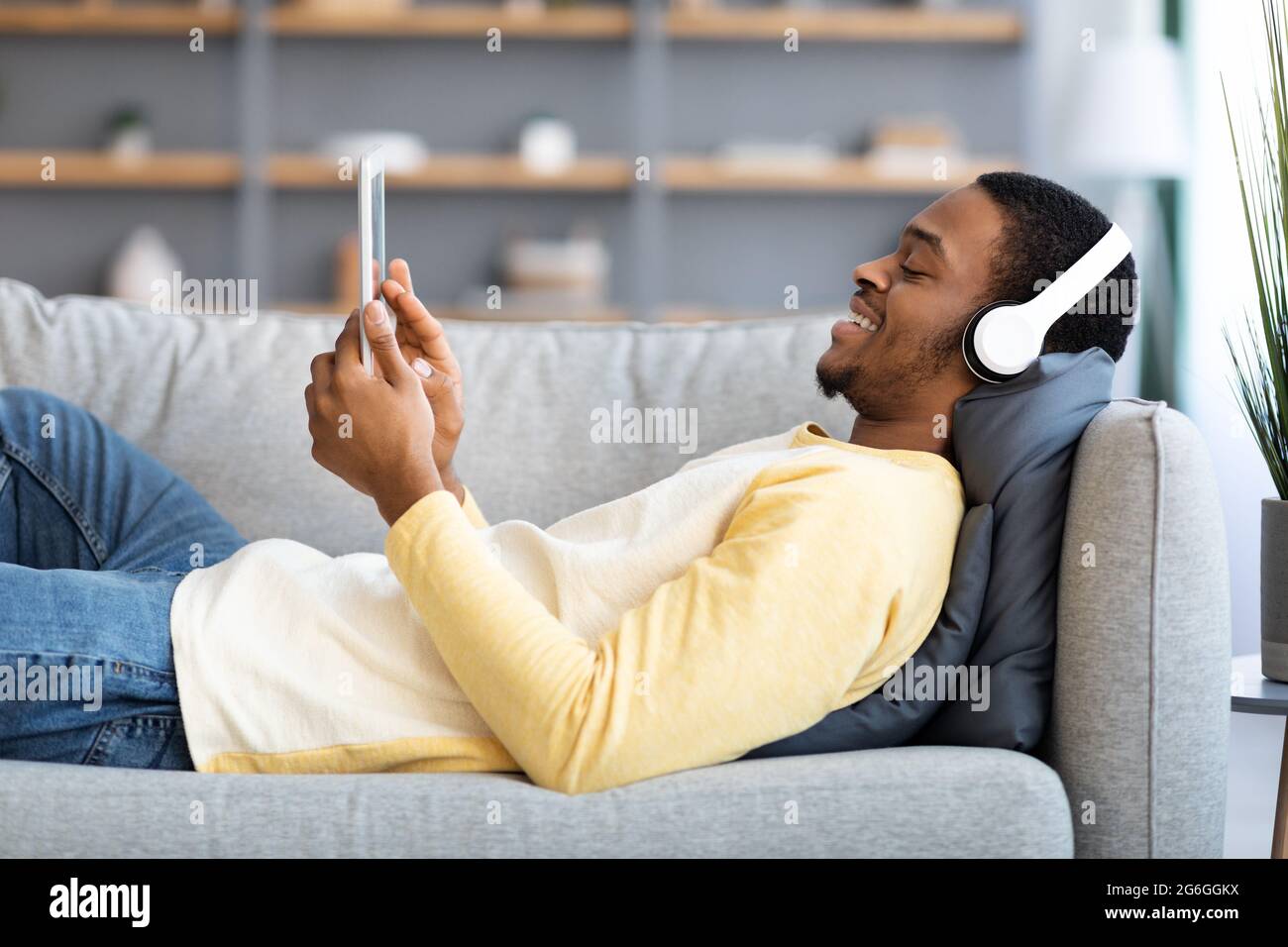 Ragazzo nero rilassato che si stende sul divano, guardando i film sul pad Foto Stock
