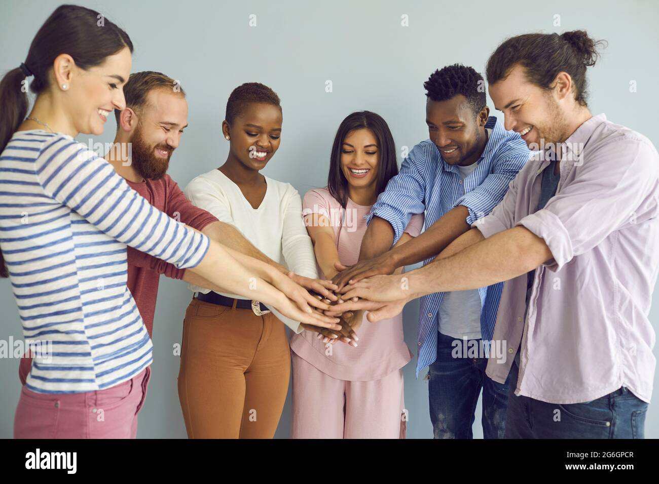 Un team di amici multinazionali, studenti o colleghi piega le braccia, simboleggiando la loro unità. Foto Stock