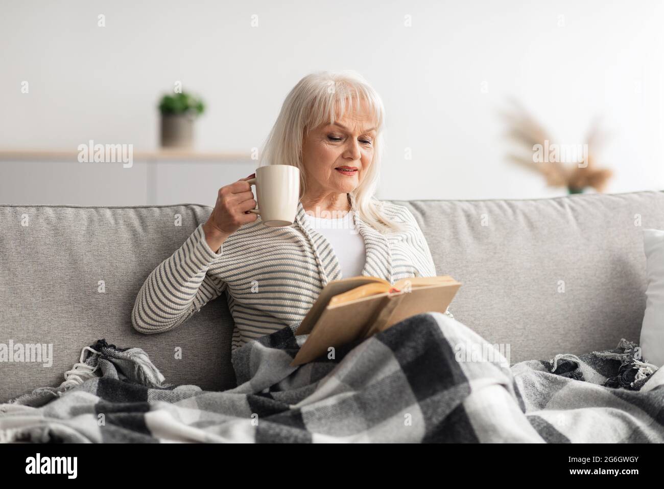 Donna matura che riposa a casa, leggendo il libro Foto Stock