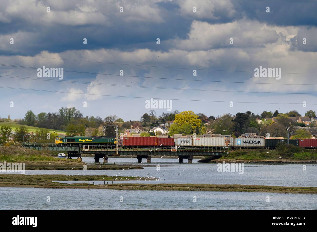 Locomotiva di classe 66 in livrea Freightliner che trasporta i contenitori di trasporto, attraversando il Viadotto di Manningtree, attraverso il fiume Stour, Essex, Inghilterra. Foto Stock