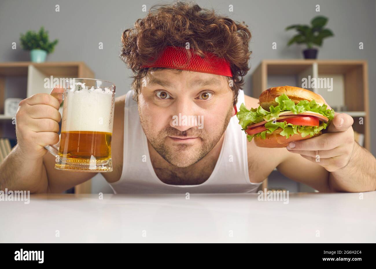 Divertente uomo grasso in abbigliamento sportivo con pinta di vetro di birra e ritratto di hamburger closeup Foto Stock