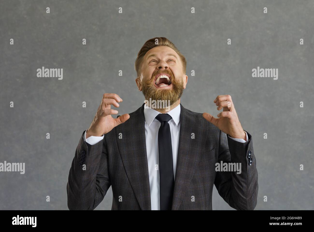 Uomo d'affari pazzo arrabbiato che guarda in su gridando con un'espressione aggressiva e le mani sollevate. Foto Stock