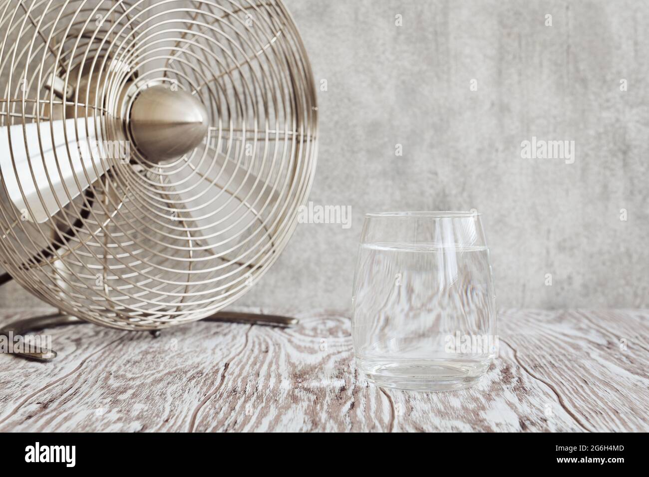 Vetro trasparente di acqua chiara e un piccolo ventilatore da tavolo su una tavola di legno closeup, profondità di campo poco profonda Foto Stock