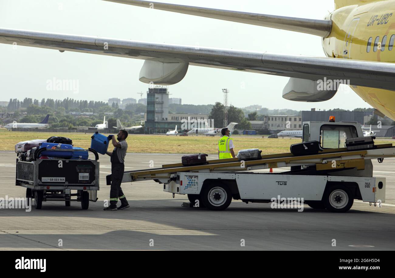 KIEV, UCRAINA - 24 GIUGNO 2021 - UN gestore di bagagli mette le valigie scaricate da un aereo su un veicolo di bagagli presso l'Igor Sikorsky Kyiv International Foto Stock