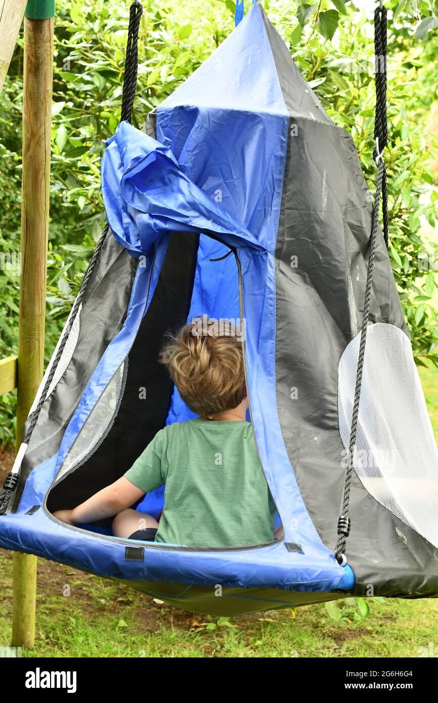 Un ragazzo seduto in una tenda altalena in un pomeriggio estivo Foto Stock