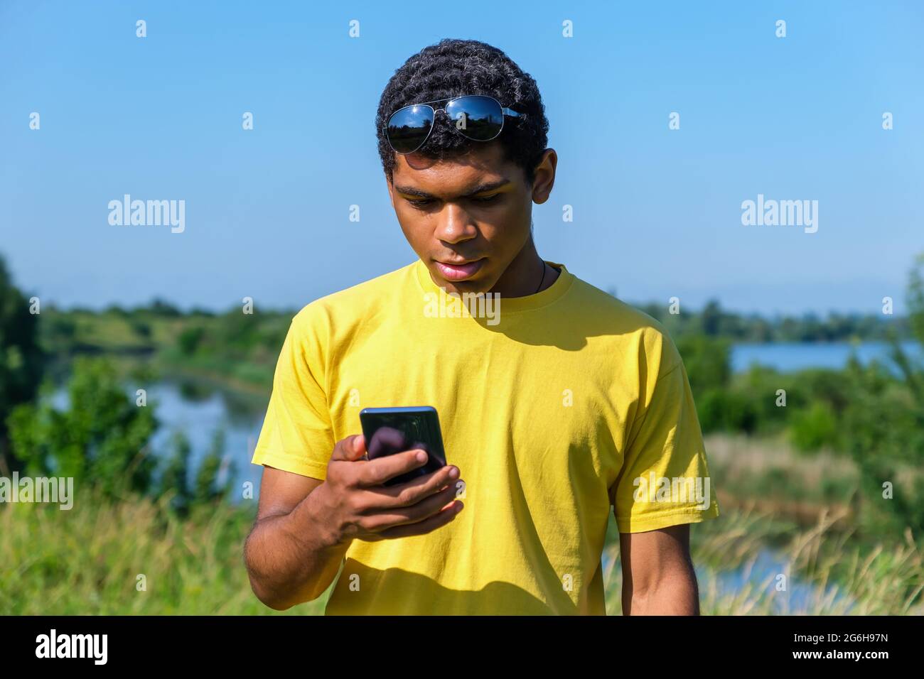 Afro-americano tipo uso telefono, chiamata e chattare online all'aperto vicino fiume Foto Stock