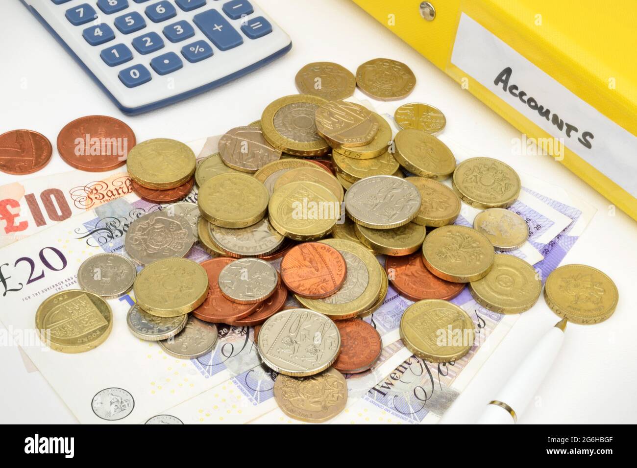 Una natura morta finanziaria con una cartella dei conti, una calcolatrice, monete, banconote e penne Foto Stock