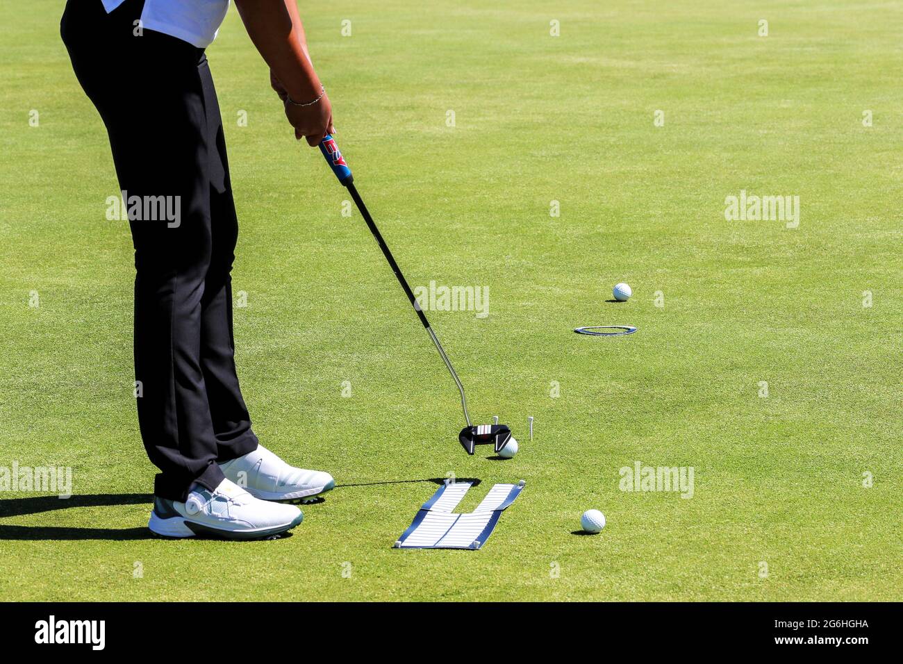 Donna golfer che pratica mettendo usando i sussidi di allineamento, i tee di golf e tre palle di golf. Foto Stock