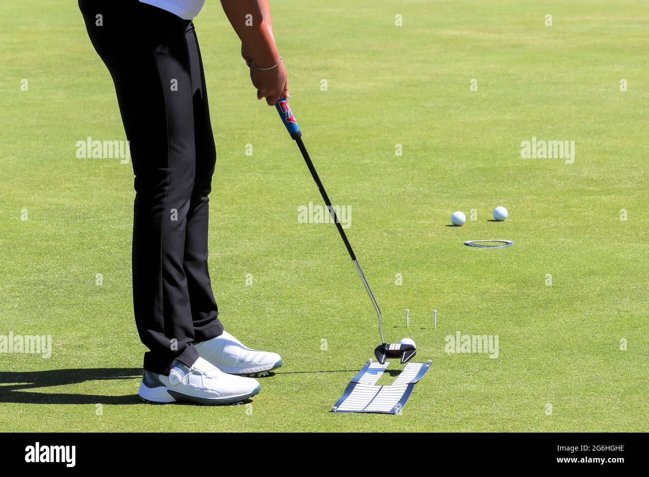 Donna golfer che pratica mettendo usando i sussidi di allineamento, i tee di golf e tre palle di golf. Foto Stock