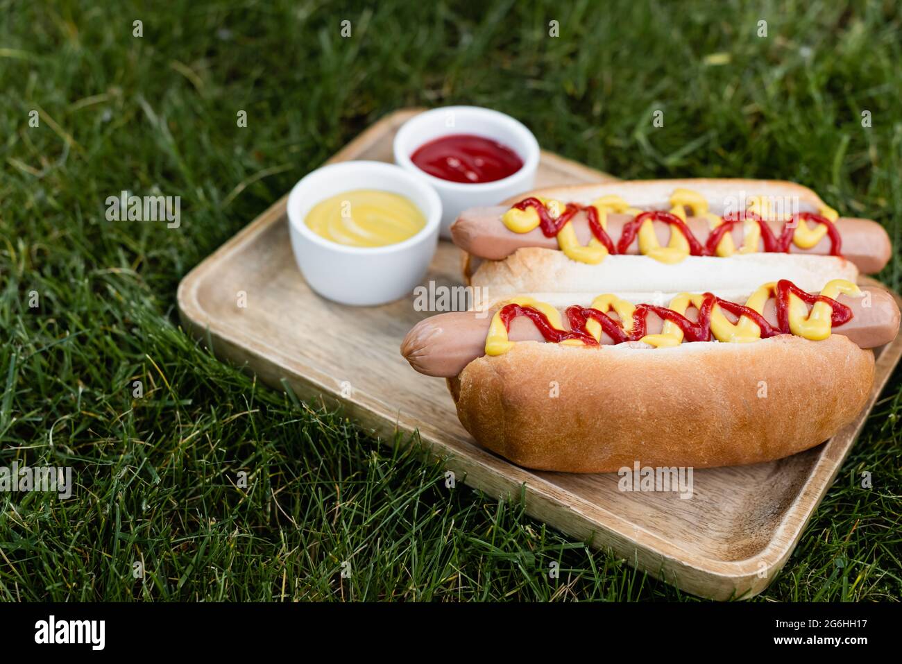 vassoio di legno con hot dog, senape e ketchup su prato verde all'aperto Foto Stock